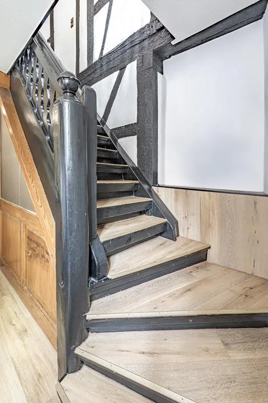 Interior view of a wooden staircase with black railings in a home with white walls and dark wood beams.