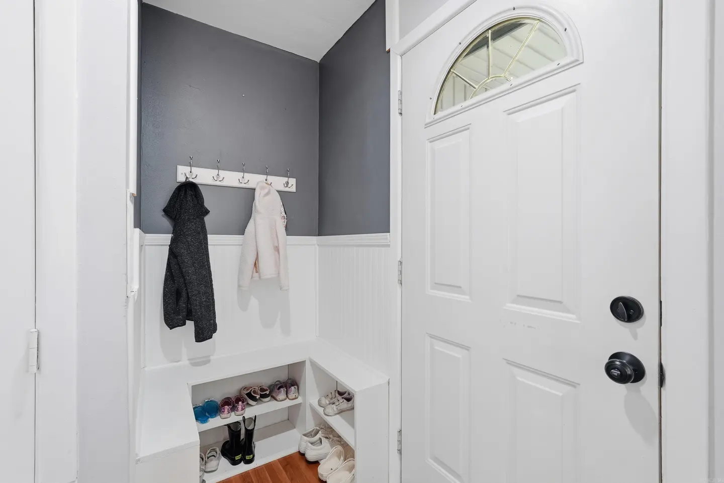 Entryway with a white door, gray walls, and a built-in bench with shoe storage. Coats hang on hooks above the bench.