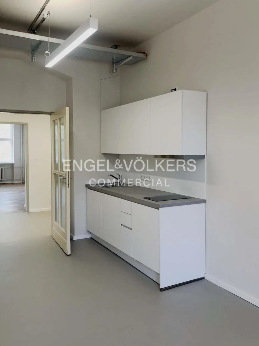 A bright, empty office space with white cabinets, gray countertops, and an open doorway. The Engel & Völkers logo is visible on the wall.