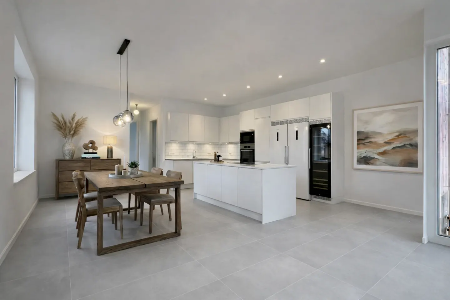 Bright, open-concept kitchen and dining area with white cabinets, island, and appliances. A wooden table with chairs sits near a sideboard with decor.