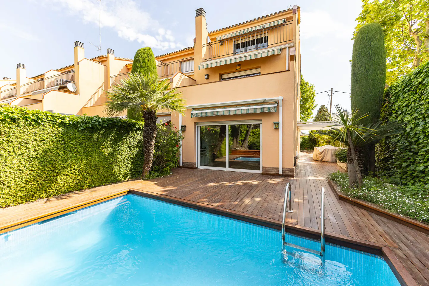 Backyard view of a peach-colored townhouse with a blue swimming pool and wooden deck.