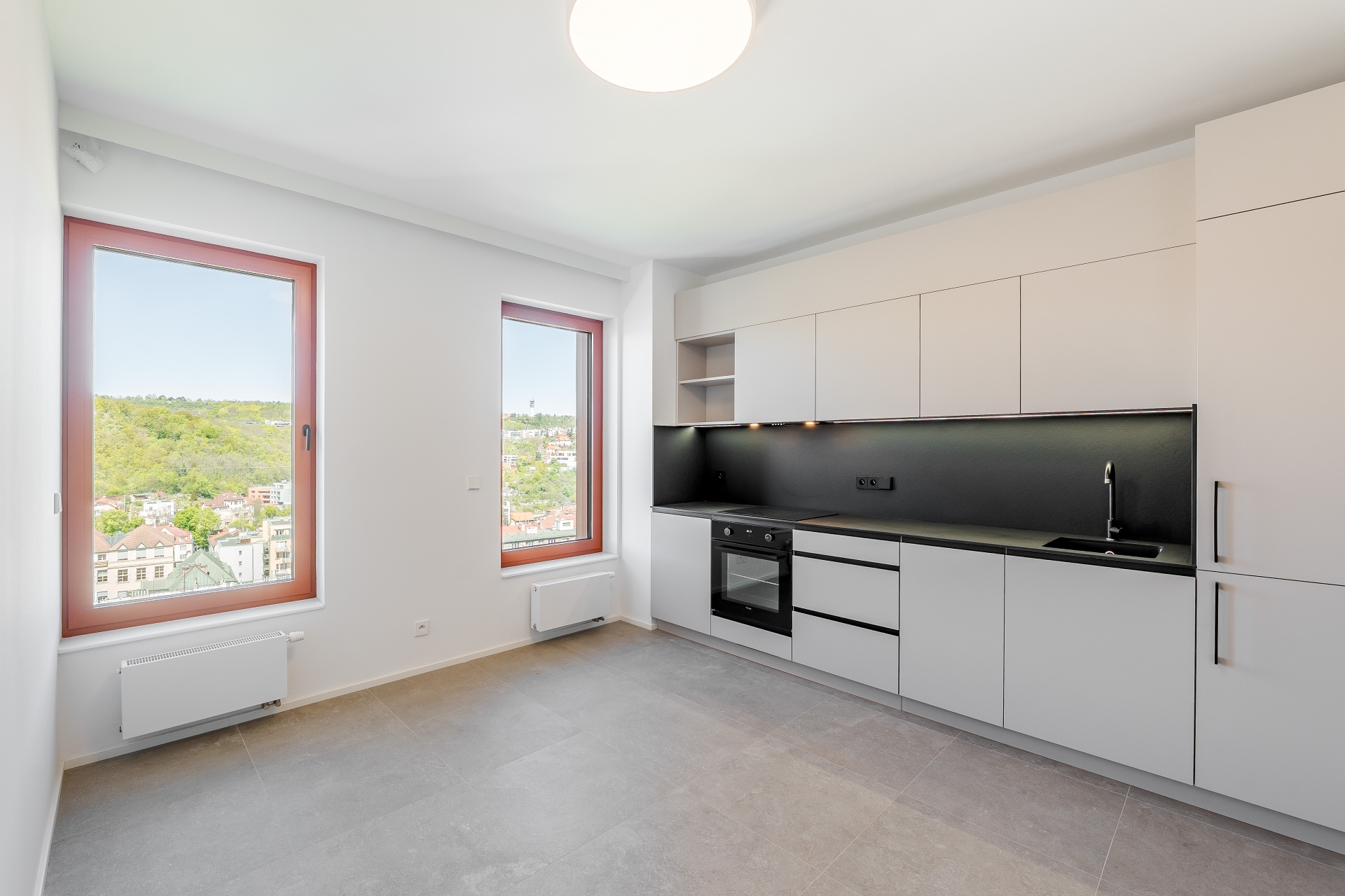 Modern kitchen with white cabinets, black backsplash, and two large windows overlooking a city and green hills. [AI-generated text]