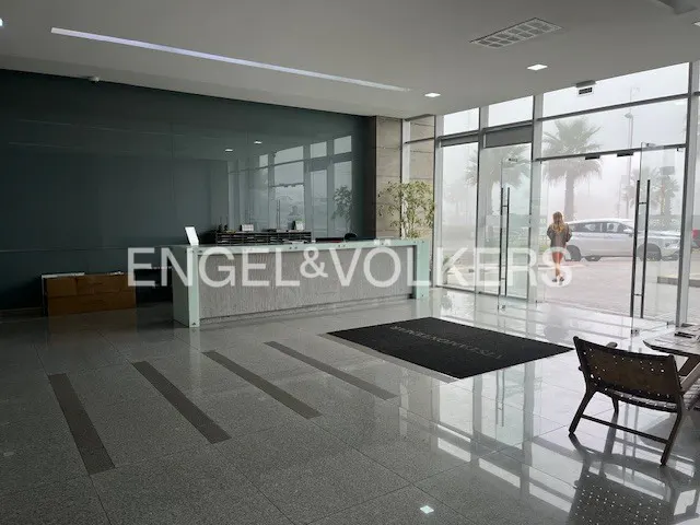 Engel & Volkers office lobby with gray tile floor, reception desk, and glass doors. A woman exits to a foggy day.