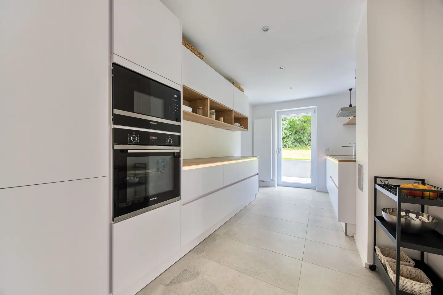 Bright, modern kitchen with white cabinets, wood countertops, and stainless steel appliances. A door leads to a green outdoor space.