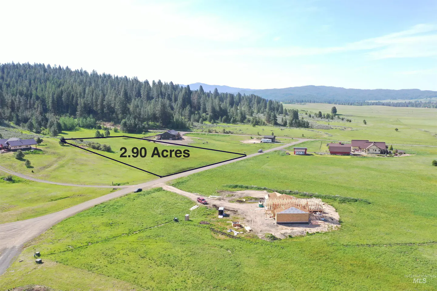 Aerial view of a 2.90 acre lot in a green, rural area with a house under construction. Forest and mountains in the background.