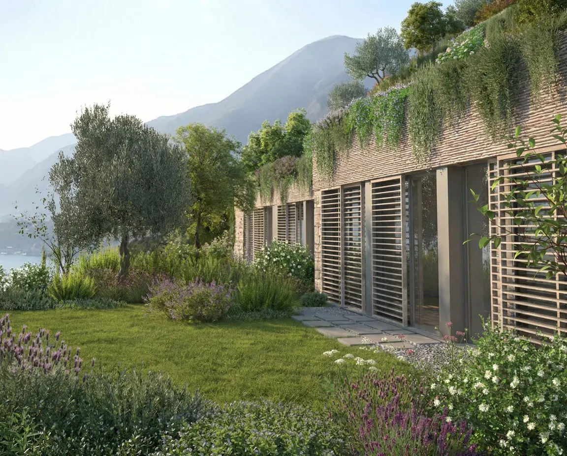 Exterior view of a modern stone house with slatted windows, a green roof, and a lush garden with mountains in the background.