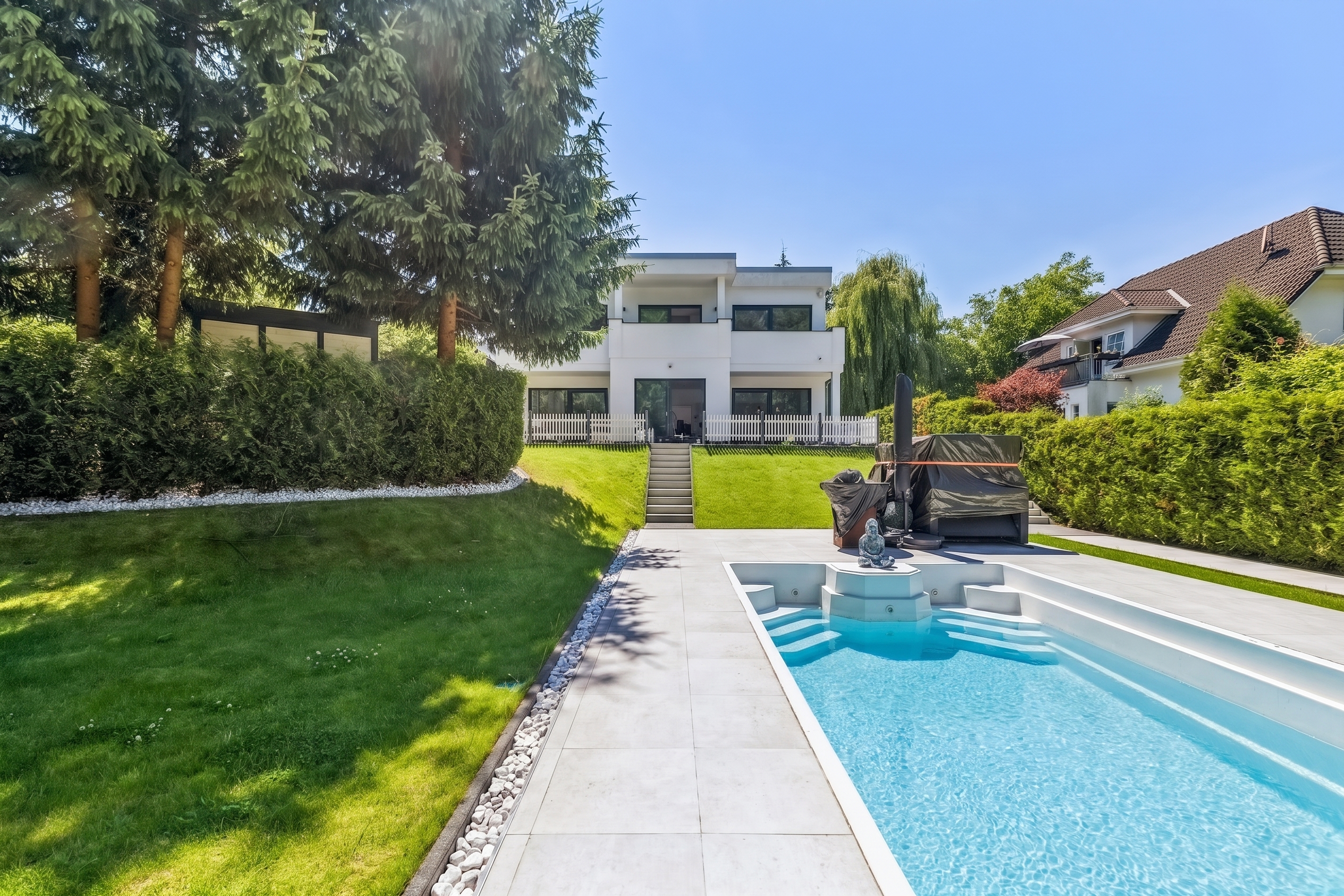 Backyard of a modern white house with a swimming pool, stone patio, green lawn, and tall privacy hedges. [AI-generated text] [KI-modifiziert]