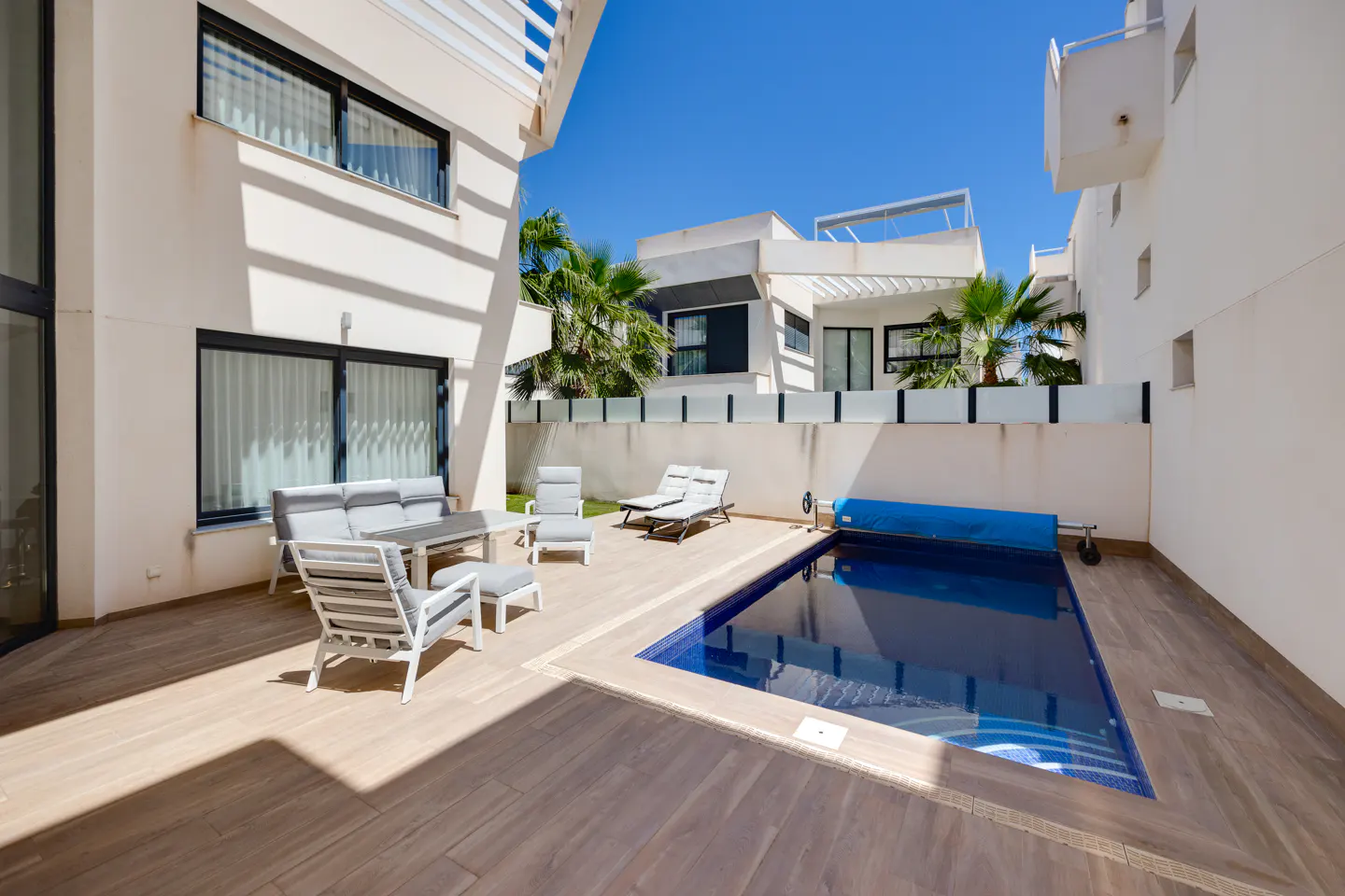 Backyard view of a modern white house with a blue tiled pool, lounge chairs, and outdoor seating.