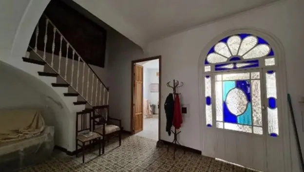 A home's entryway features a staircase, chairs, and a stained-glass door. A coat rack with garments stands near the door.