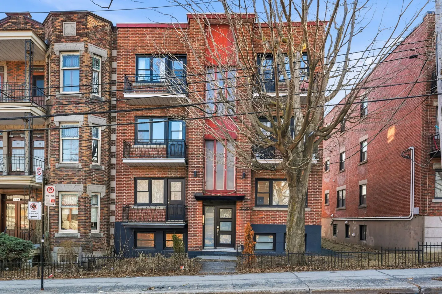 Exterior view of a three-story brick apartment building with black trim and a red accent stripe.