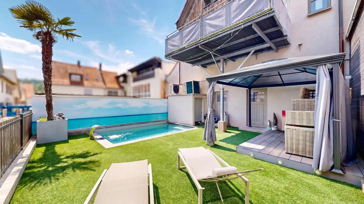 Backyard with a small pool, palm tree, and two lounge chairs on green turf. A gazebo stands near the building.