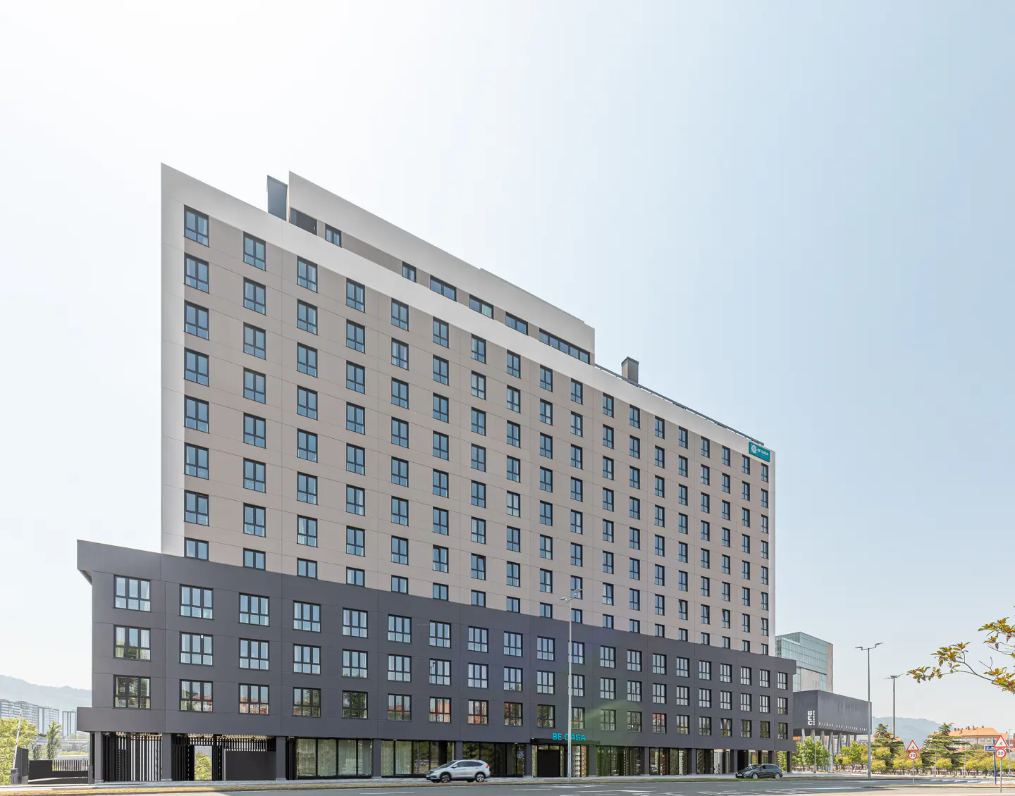 Exterior view of a modern, multi-story hotel with gray and white facade, many windows, and a street view.