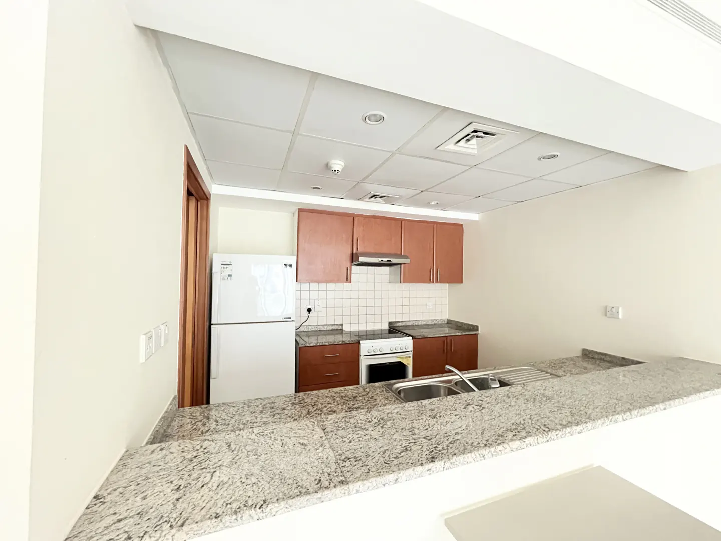 A bright kitchen with brown cabinets, white appliances, and a speckled granite countertop.