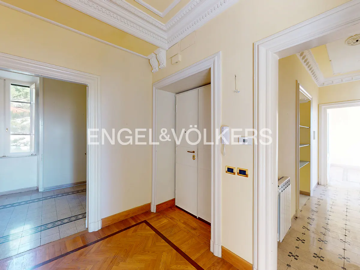 Bright hallway with cream walls, white trim, ornate crown molding, hardwood floors, and multiple doorways.
