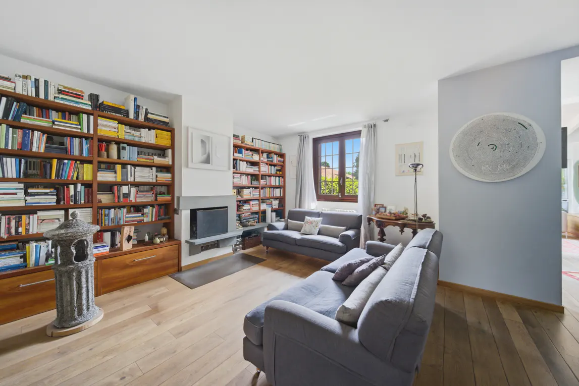 A bright living room with hardwood floors, two gray sofas, and floor-to-ceiling bookshelves filled with books.