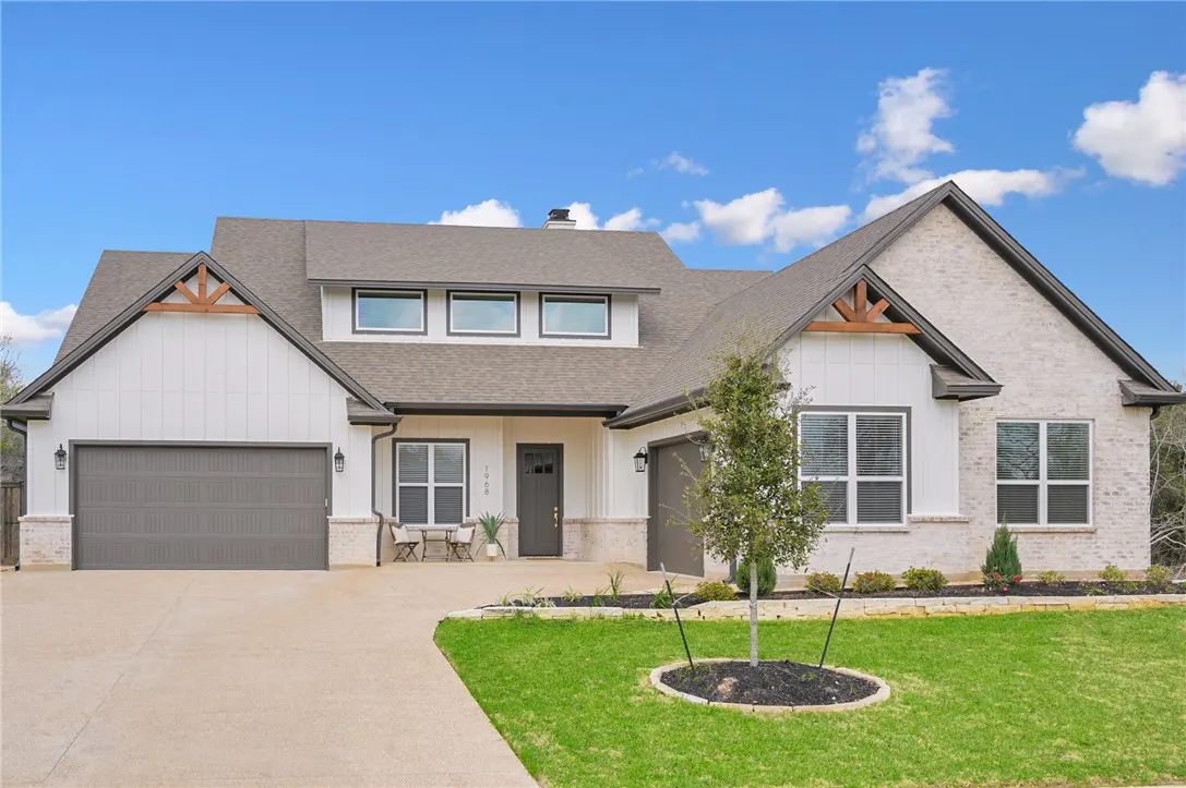 Two-story house with white siding, gray brick, and a gray roof under a blue sky. A gray garage door is on the left.