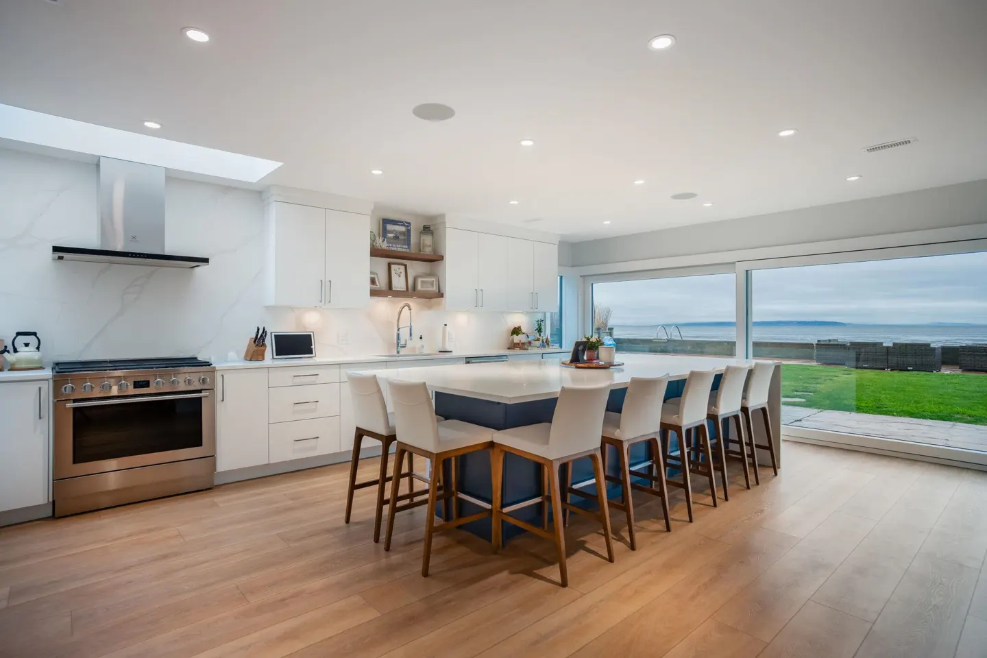 Bright, modern kitchen with white cabinets, stainless steel appliances, and a large island with seating overlooking an ocean view.