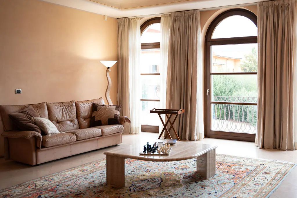 Living room with a brown leather sofa, marble coffee table with chess set, and arched windows with beige curtains.