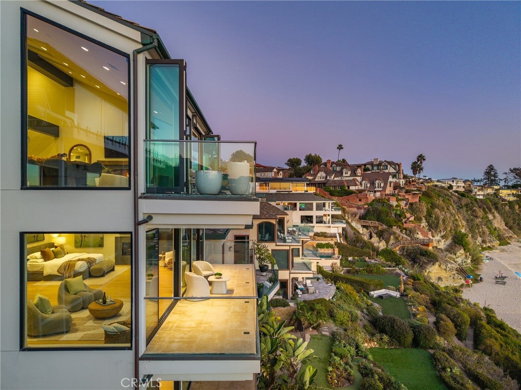 Modern multi-story home with glass balconies overlooking a coastal cliffside and beach at sunset. [AI-generated text]