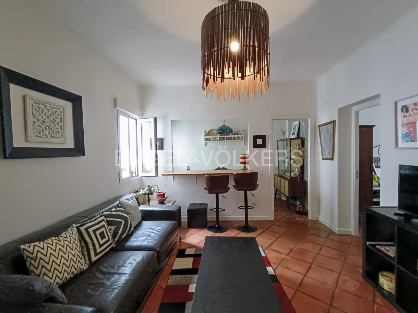 Living room with dark leather sofa, patterned pillows, black coffee table, and a breakfast bar with two stools.