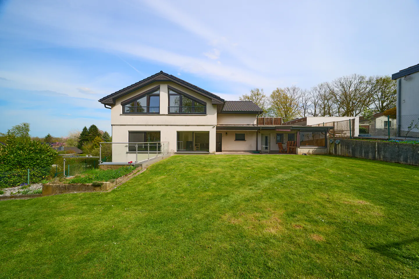 Two-story house with a large green lawn. The house has a dark roof and large windows.
