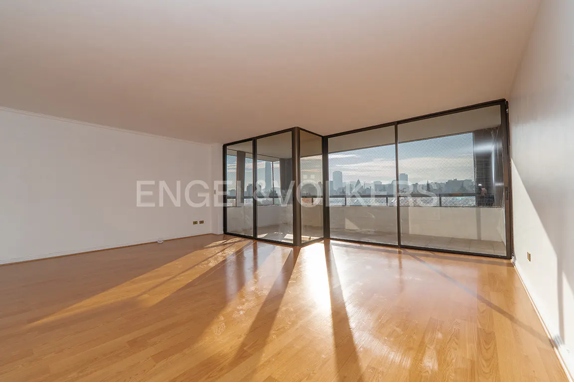Bright, empty room with hardwood floors and white walls. Large windows offer a city view. Sunlight streams in, creating long shadows.