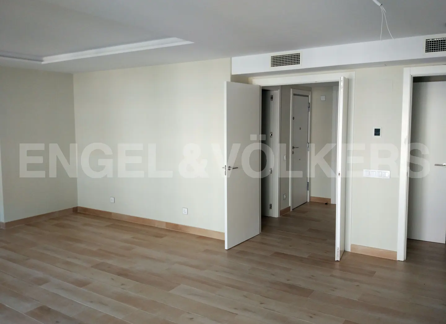 Unfurnished room with light wood floors, white walls, and multiple white doors. Engel & Völkers logo is visible on the wall.