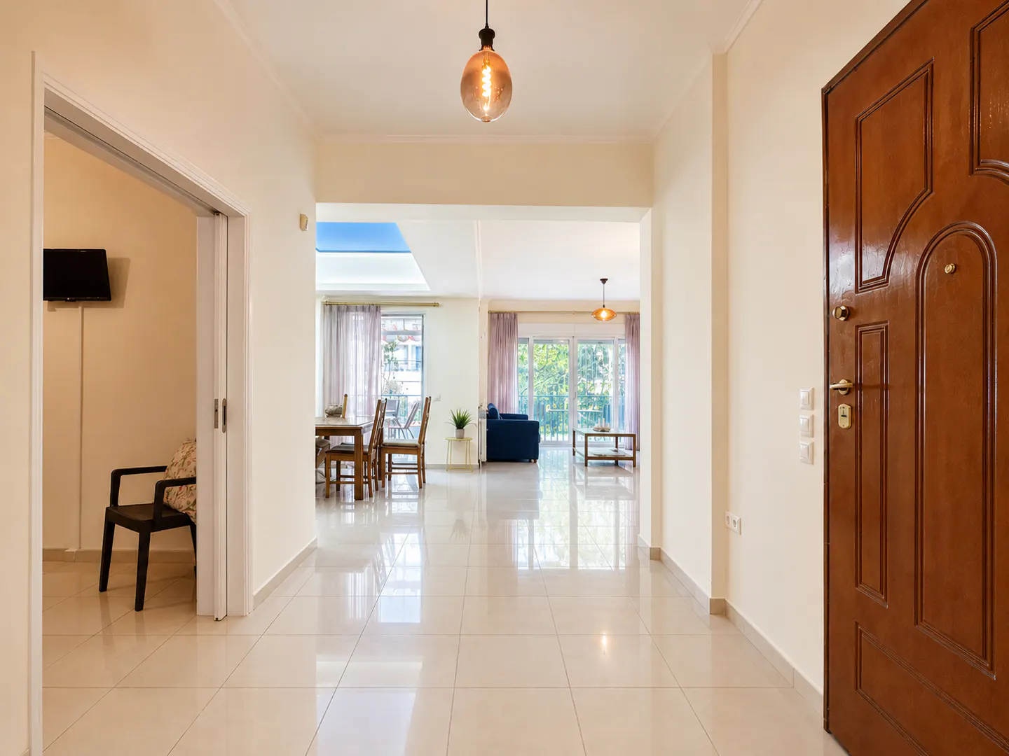 Hallway view of a home with beige tile floors, a brown front door, and an open living and dining area.