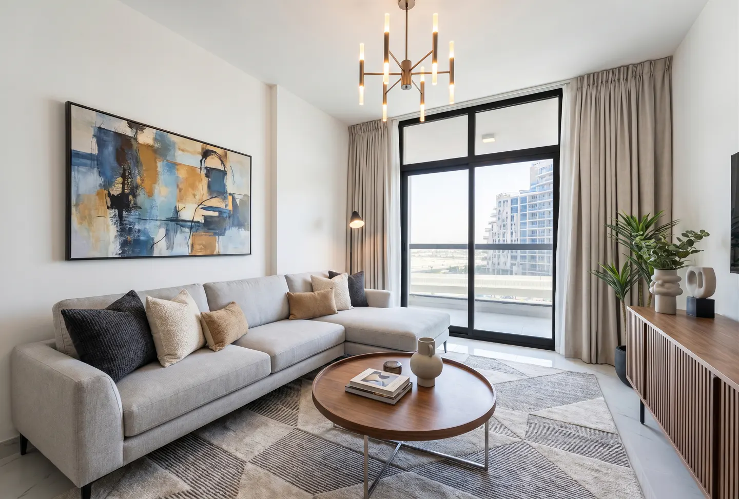 Bright living room with a gray sectional sofa, round wood table, and abstract art. Large windows offer a city view.