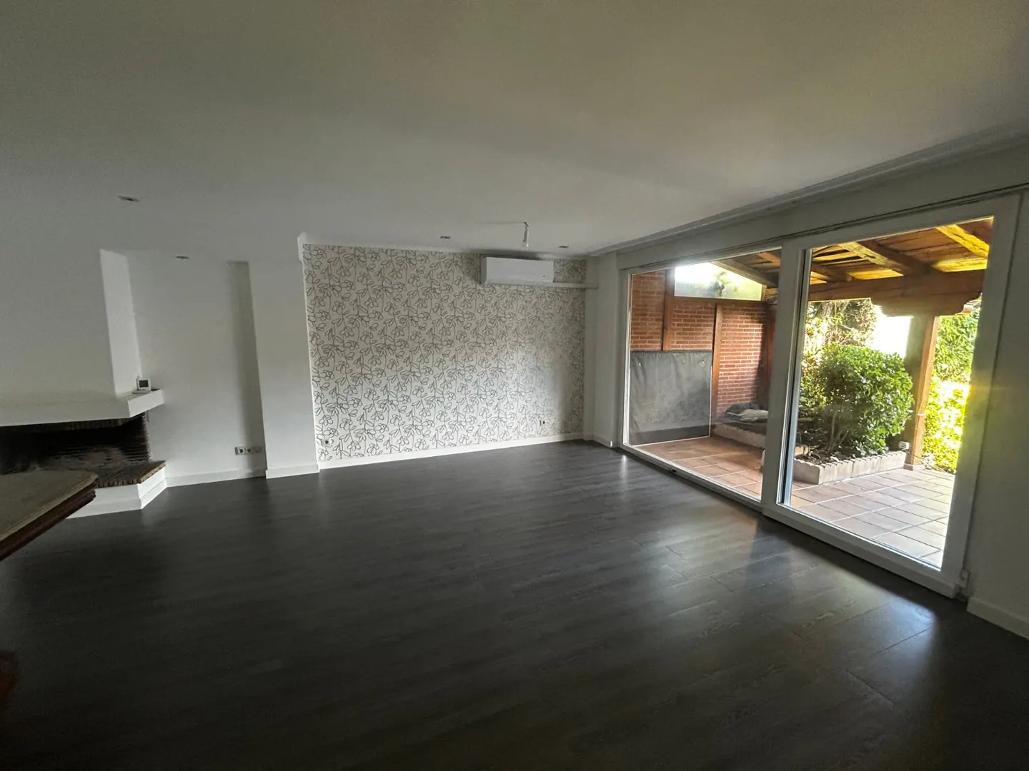 Spacious living room with dark wood floors, patterned wallpaper, a fireplace, and large sliding doors to a patio.
