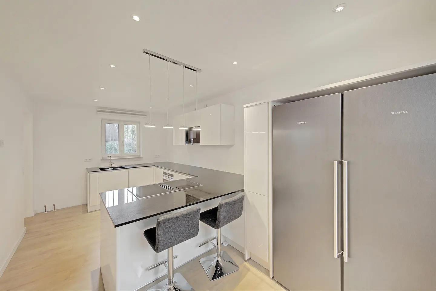 Bright, modern kitchen with white cabinets, black countertops, and stainless steel appliances. Two gray bar stools sit at the island.