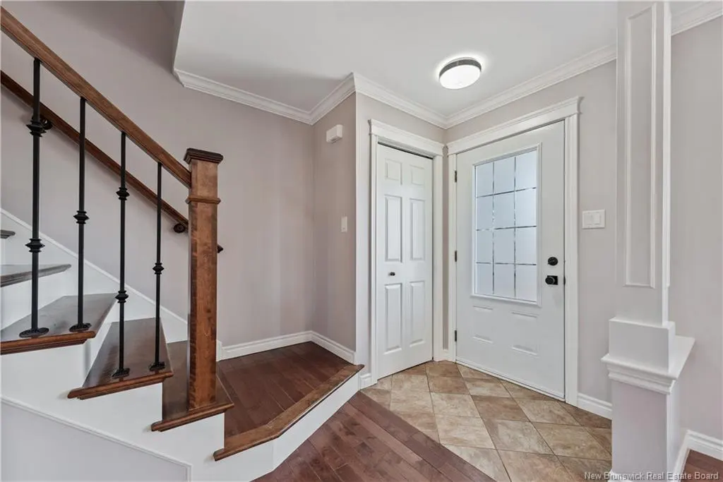 Foyer with stairs, wood and iron railing, white doors, and diamond-patterned tile floor. Walls are light gray.