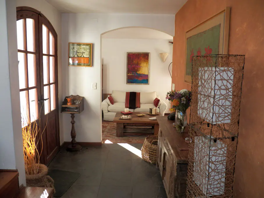 A home's entryway with a wooden door, table, and a view into the living room with a white sofa and colorful artwork.