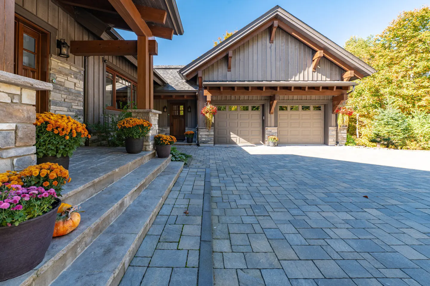Exterior of a two-story house with a gray stone and wood facade, a two-car garage, and a stone driveway. Orange flowers decorate the porch.