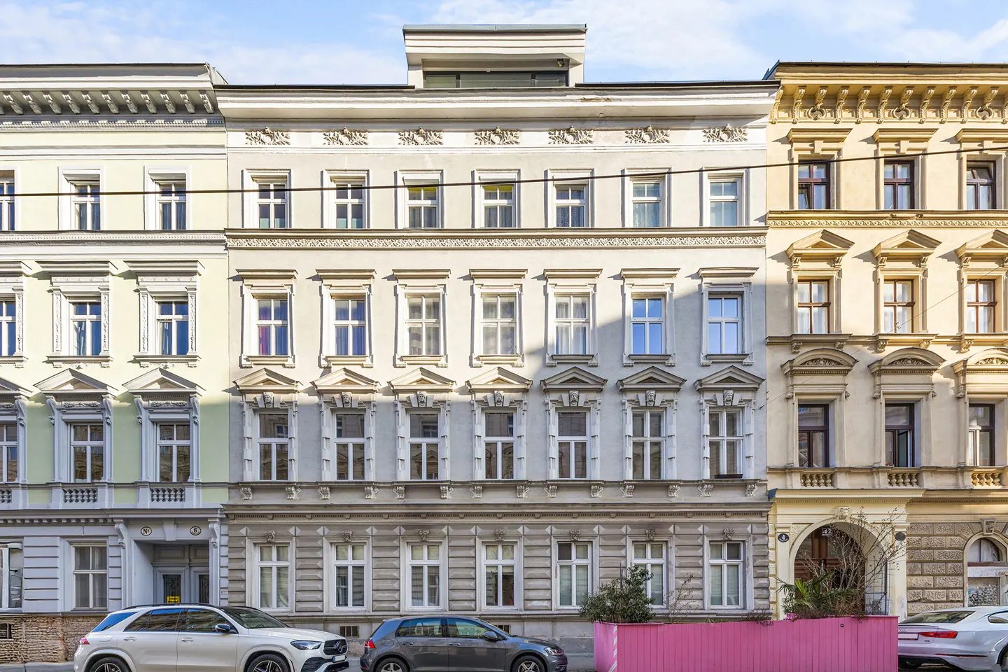 Facade of three ornate, multi-story buildings with many windows. Cars are parked on the street in front.