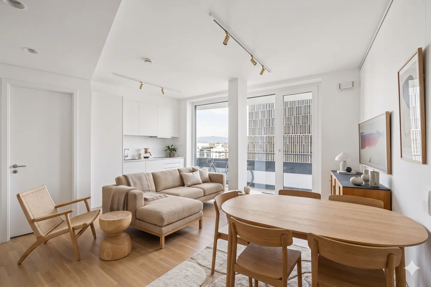 Bright, modern apartment with a beige sectional sofa, wood dining table, and white kitchen. Large windows offer city views.