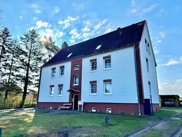Exterior view of a three-story white building with a dark roof and red brick accents, set against a blue sky with scattered clouds.