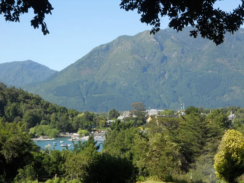 Scenic view of a lake with boats, surrounded by green trees and mountains under a blue sky.