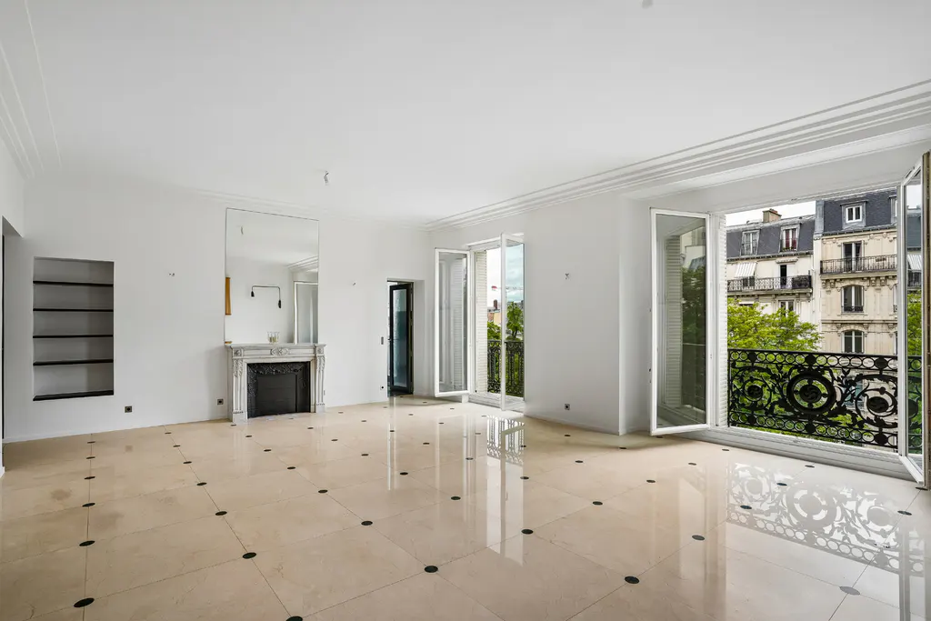 Bright, empty living room with white walls, polished beige tile floors, a fireplace, and balcony doors overlooking a city.