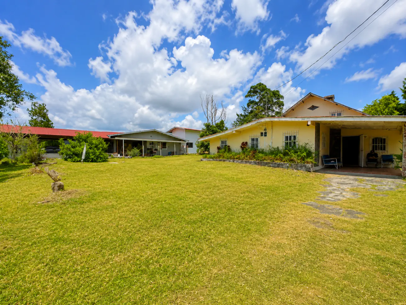 A yellow house with a large green lawn under a blue sky with white clouds.