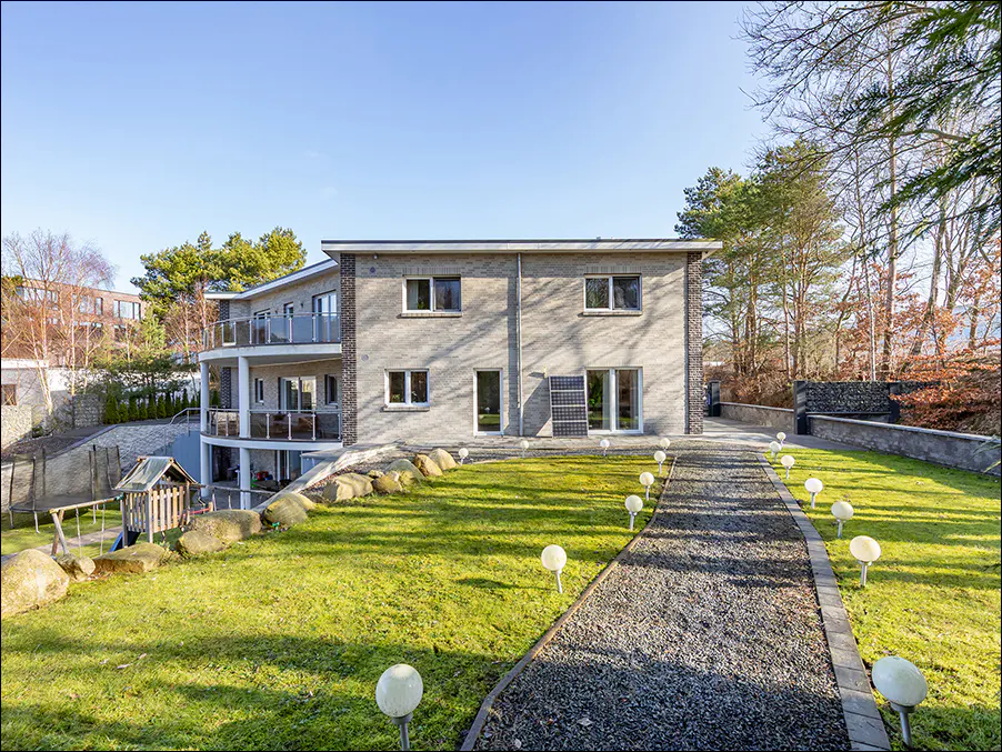 Two-story gray brick house with a gravel path lined with globe lights. Green lawn and trees surround the property.