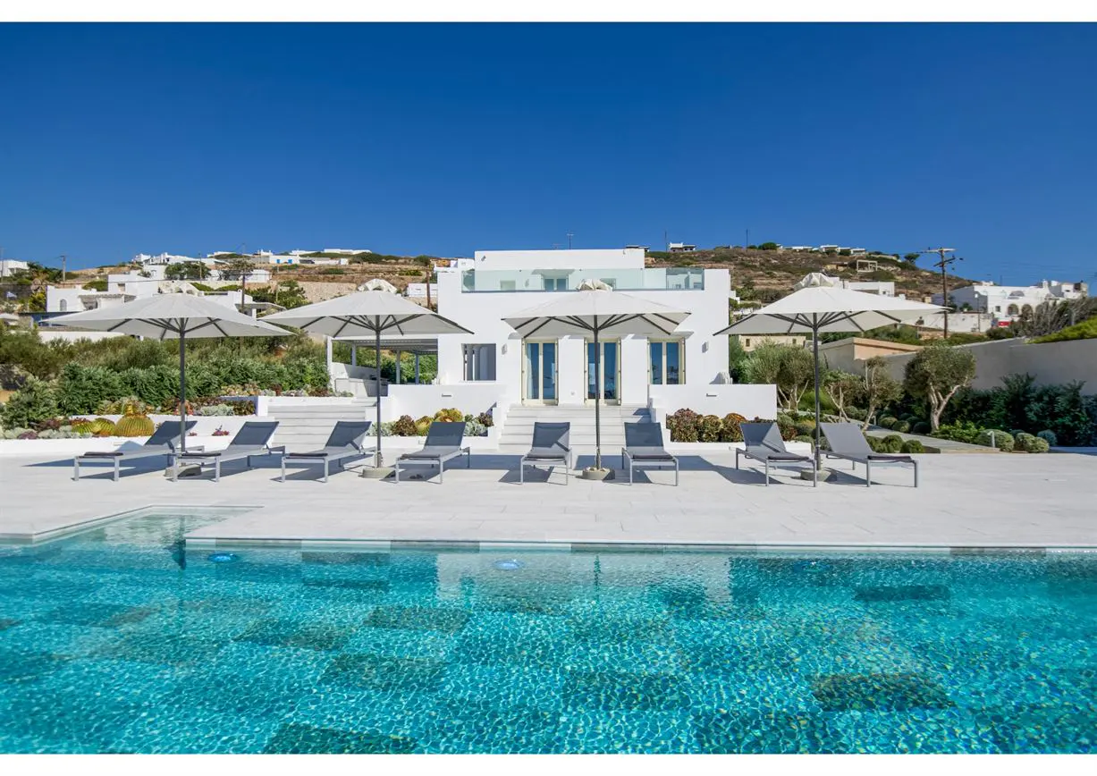 Luxury villa with pool. White building with lounge chairs and umbrellas. Blue sky.