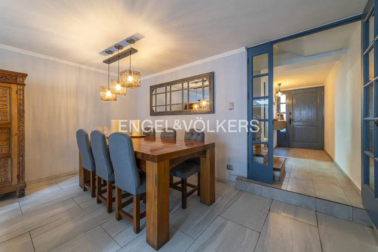 A dining room with a wooden table, six blue chairs, and a decorative light fixture. A blue door leads to another room.