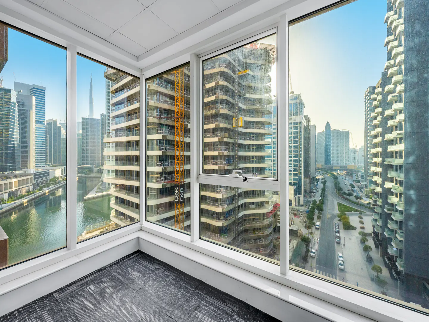 Corner room view through large windows of Dubai skyline, including Burj Khalifa, buildings, and a canal.