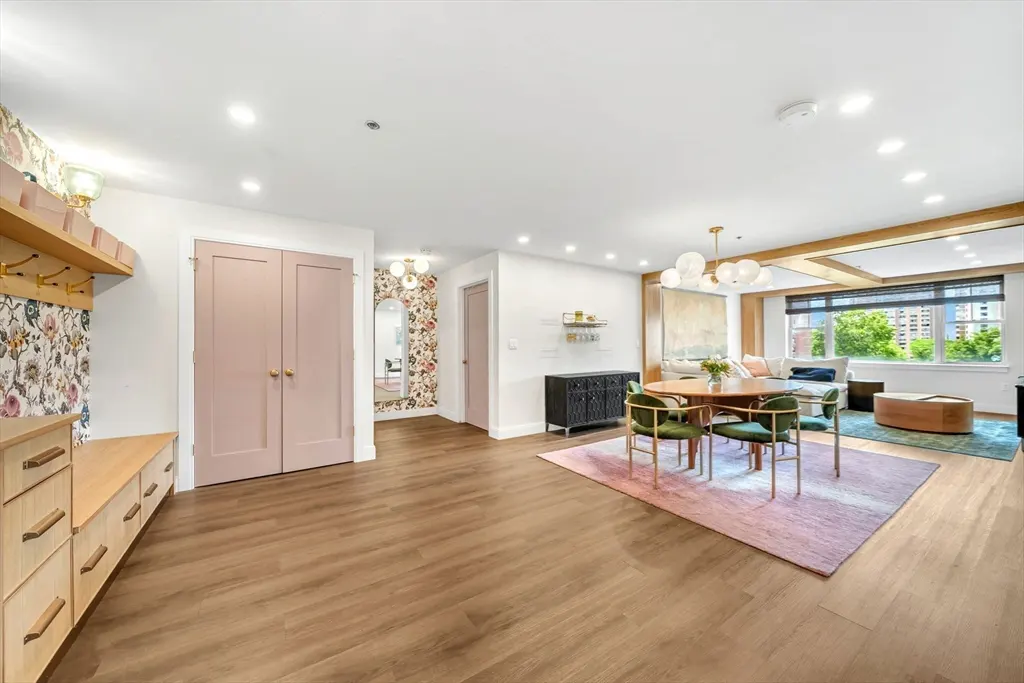 Open-concept living area with light wood floors, pink double doors, a dining table with green chairs, and floral wallpaper.