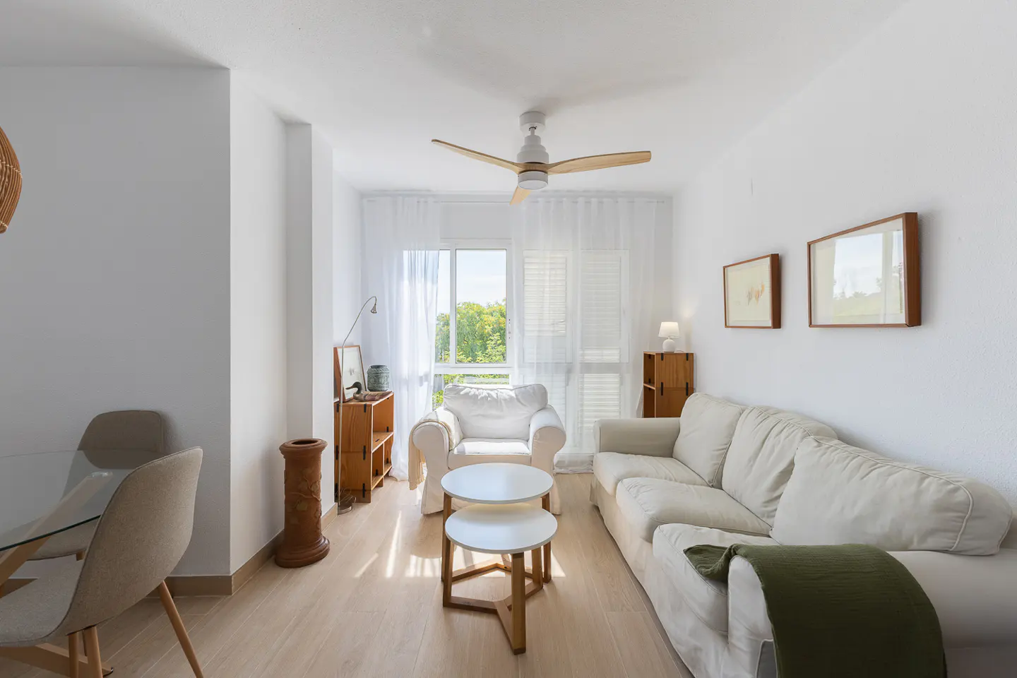 Bright living room with white sofa, two round coffee tables, armchair by window, and light wood flooring.