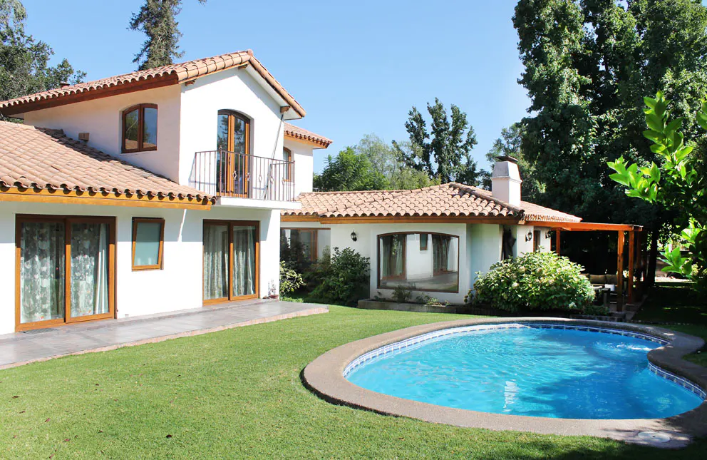 Two-story white house with a red tile roof, a blue pool, and green grass on a sunny day.