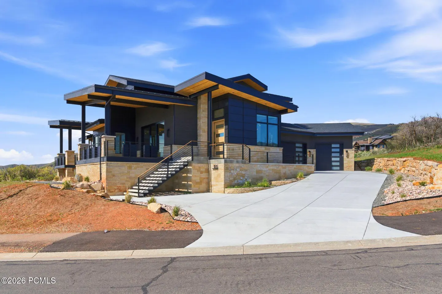 Modern two-story home with a gray exterior, stone accents, and a concrete driveway under a blue sky.