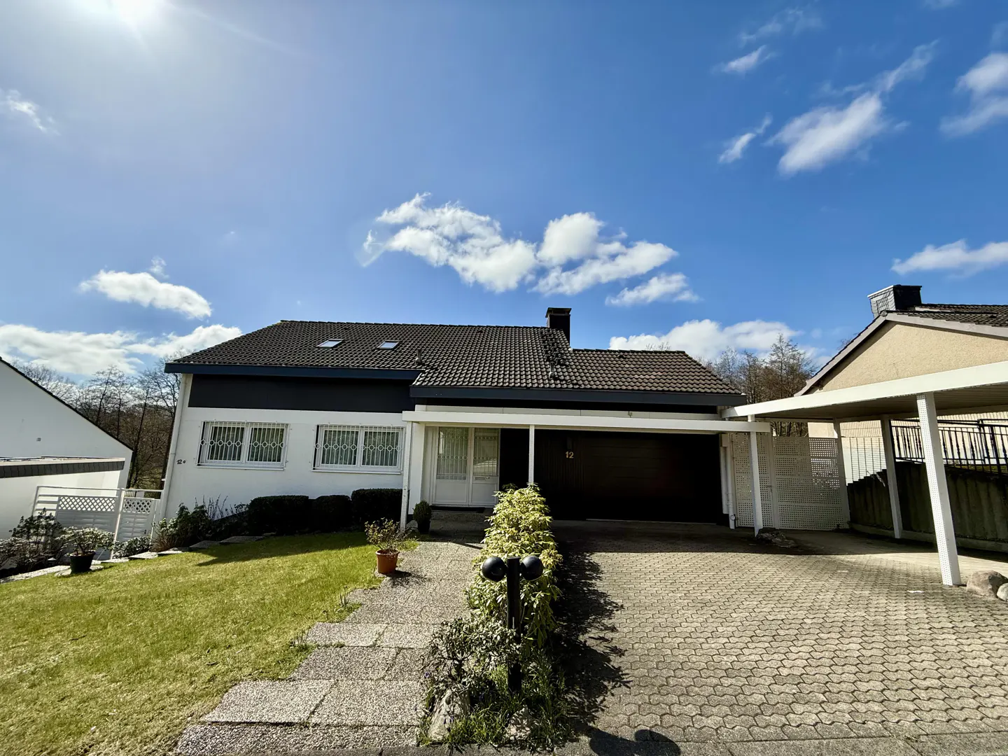 Exterior of a one-story house with a dark roof, white walls, and a black garage door on a sunny day.