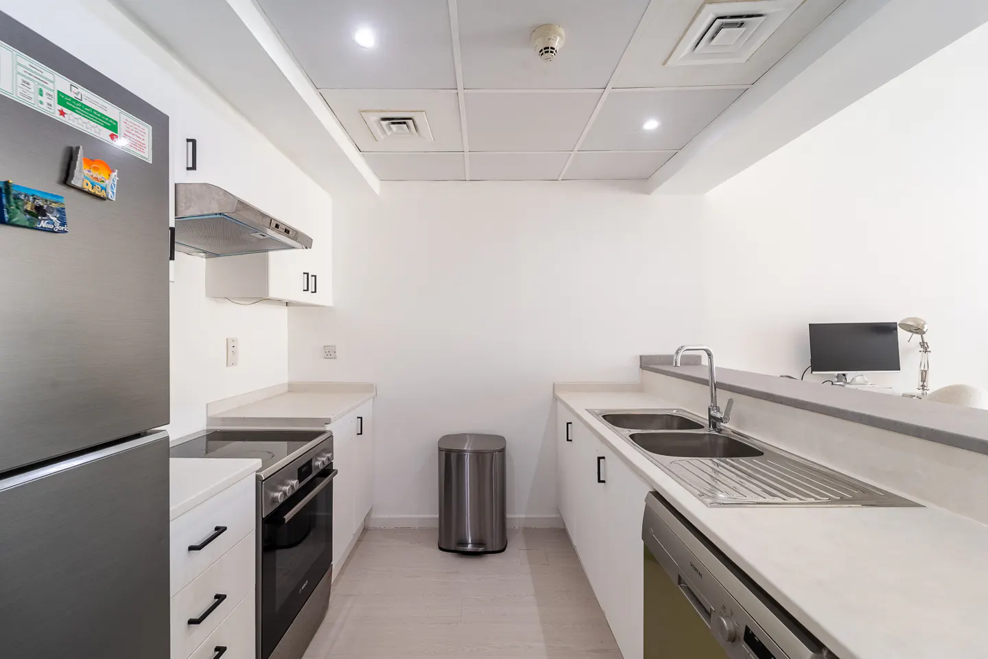 Bright, modern kitchen with white cabinets, stainless steel appliances, and a double sink. A computer sits on a counter in the background.